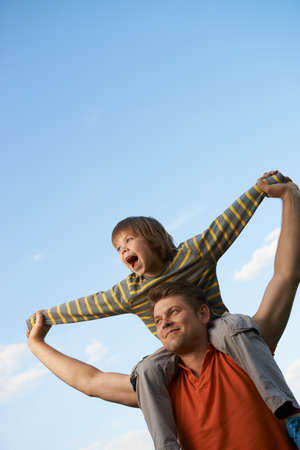 Happy son on the shoulders of the father. On the background of blue skyの写真素材