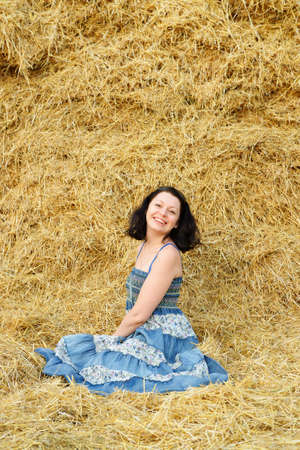 A young attractive woman on the background of the large stack of hayの写真素材