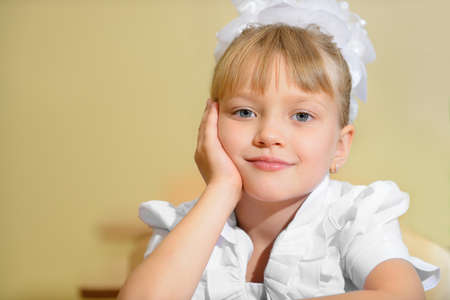 Happy schoolchild with white bows. Sitting at a Deskの写真素材
