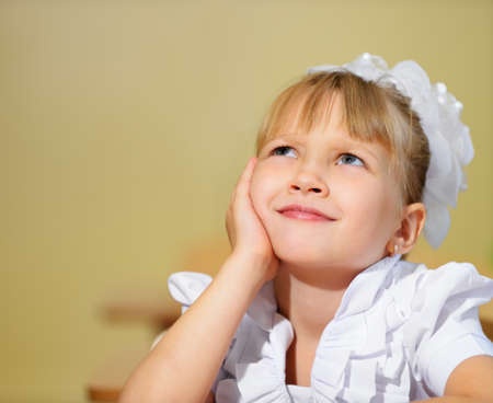 Thoughtful schoolchild with white bows. Sitting at a Deskの写真素材