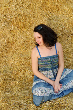 A young attractive woman on the background of the large stack of hayの写真素材