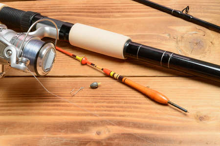Objects for fishing. The rod with reel, a float, fishing line and hook on a wooden surfaceの写真素材