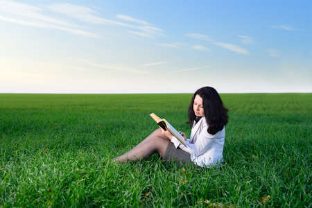 The girl in a business suit reads the book. Sitting on a green meadowの写真素材