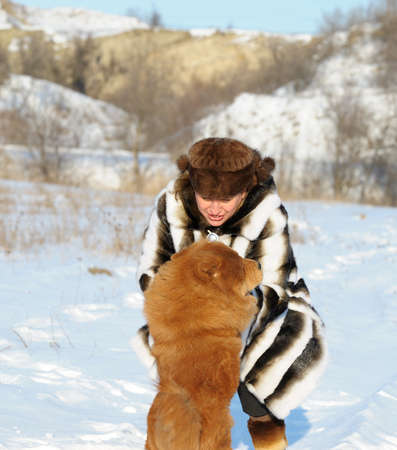 The woman in a mink fur coat plays with a dog. Winter weatherの写真素材