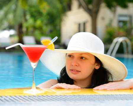 girl with a cocktail at the edge of the swimming pool . Red cocktail with an orange slice.の写真素材
