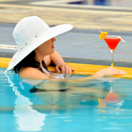 girl with a cocktail at the edge of the swimming pool . Red cocktail with an orange slice.の写真素材