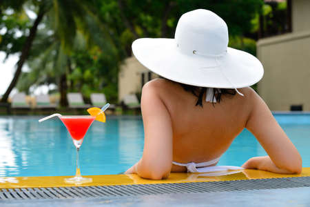 girl with a cocktail at the edge of the swimming pool . Red cocktail with an orange slice.の写真素材