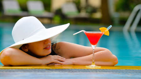 girl with a cocktail at the edge of the swimming pool . Red cocktail with an orange slice.の写真素材