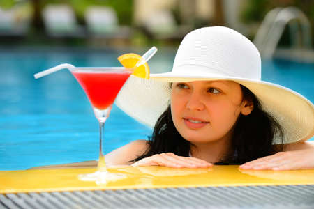 girl with a cocktail at the edge of the swimming pool . Red cocktail with an orange slice.の写真素材
