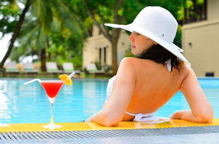 girl with a cocktail at the edge of the swimming pool . Red cocktail with an orange slice.の写真素材