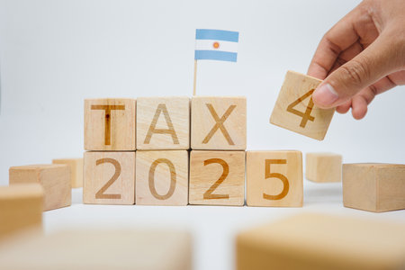 Wooden blocks arranged to showcase 'Tax 2025' with an Argentine flag and a person's hand rearranging a block, symbolizing financial strategy, taxation planning, and national focus in Argentinaの写真素材