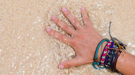 Women Hand with Colourful Wristband Toching Wet Sand on the Beachの写真素材