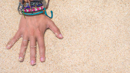 Women Hand with Colourful Wristband Toching Wet Sand on the Beachの写真素材