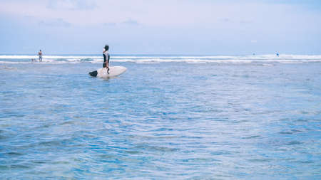 Silhouette of Fit woman going to surf in sea and looking to wave edge on horizon at Bali island,...