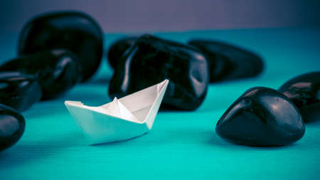 Lonely White Paper Ships between Abstract Black Rock Stones on Blue Background. Blue-Violet Coloursの写真素材