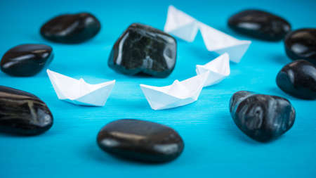 White paper boats in sigle file between abstract rock stones on blue backgroundの写真素材