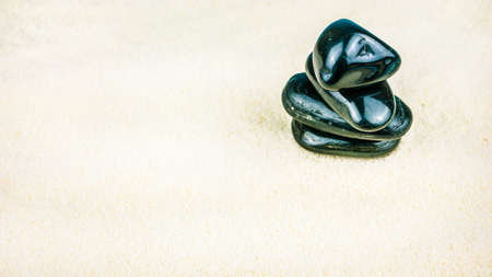 Growing piled up of four black pebbles on bright white sand
