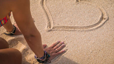 Young Woman Looking at Drawed Heart Shape in Sand on the Beach, Baliの写真素材
