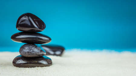 Growing piled up of four black pebbles on bright sand with blue backgroundの写真素材