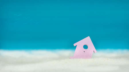 Symbol of little lilac house on the sand with bright blue painted sky backgroundの写真素材