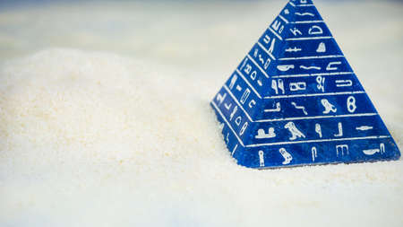 Abstract blue pyramid with hieroglyph staying on sandの写真素材