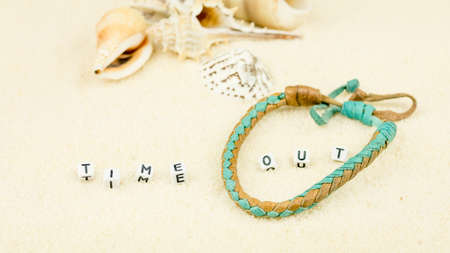 Time out letters in front of sea shells and coloured wristbandon on sandy beachの写真素材