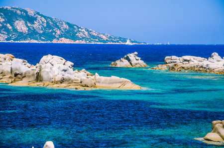 Granite rocks in sea, amazing azure water, white sailboat in background near Porto Pollo, Sardinia, Italyの写真素材