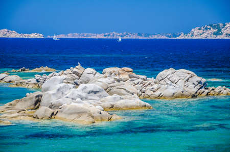 Granite rocks in sea, amazing azure water, white sailboat in background near Porto Pollo, Sardinia, Italyの写真素材