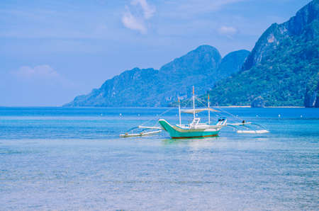 White banca boat in calm blue ocean, Seven Commandos Beach in background, El Nido, Philippinesの写真素材