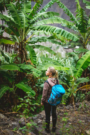 Blond yong women with blue backpack admire banana plantation on the trekking route to paul valley on santo antao island, cape verdeの写真素材