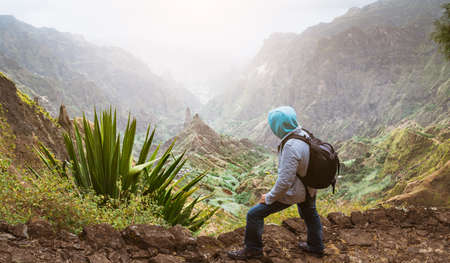 Traveler with backpack looking over the rural landscape with mountain peaks and ravine in dust air on the path from Xo-Xo Valley. Santo Antao Island, Cape Verdeの写真素材