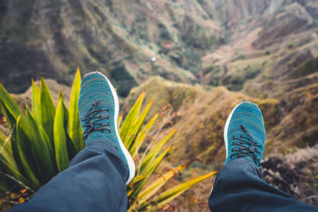 Feet of traveler streching down his legs over breathtaking mountain landscape with mountain peaks, rugged cliffs on Santo Antao Island, Cape Verde. Agave underneathの写真素材