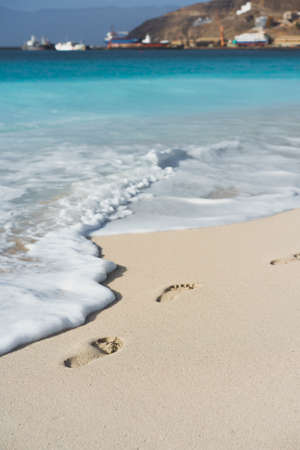 Ocean waves rolling to the foot prints on the tropical beach with azure waterの写真素材