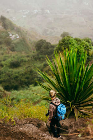 Woman with camera and backpack near one huge agave plant with arid landscape of location called Corda in background. Santo Antao island, Cabo Verdeの写真素材