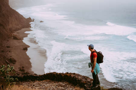 Tourist walking long way along cliff coastline with ocean waves from Cruzinha to to Ponta do Sol. Huge mountains on the trekking path. Santo Antao Island, Cape Verdeの写真素材
