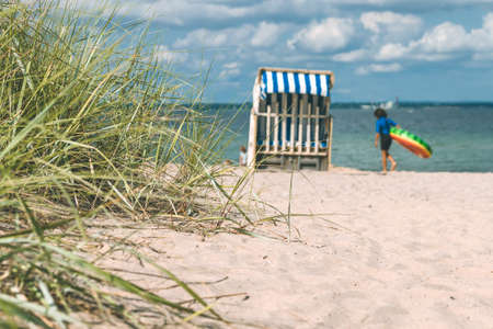 Sand dune with grass and blue colored roofed chairs on sandy beach and blurred kids in Background. Travemunde. Germanyの写真素材