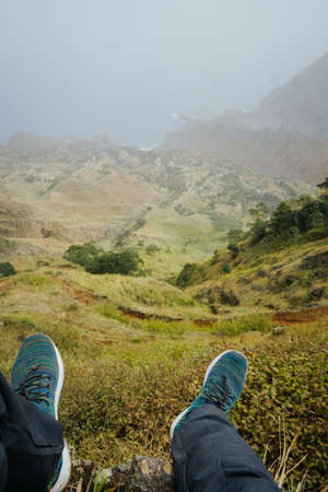 Traveler legs over verdant valley lead to ocean coastline. Santo Antao Island, Cape Verdeの写真素材