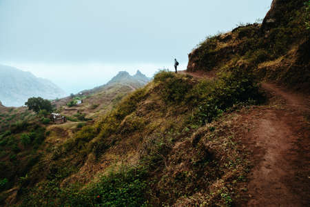 Hiker silhouette looks into the valley and listens to the silence. Fog and mist hang over the mountain peaks on the trail to Pompas. Santo Antao Cape Verdeの写真素材