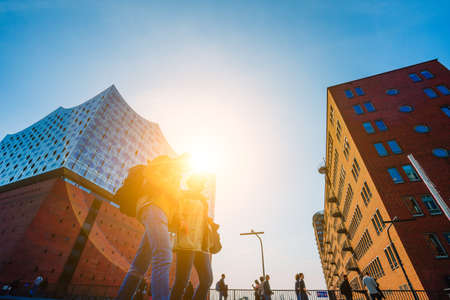 Hamburg, Germany - May 17, 2018: Elbphilharmonie, Panoramic shot - blue sky and bright sun light and flares from behind, Tourists in front, Hamburg, Germanyのeditorial素材