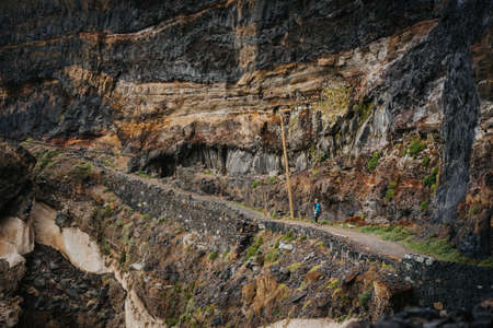 Tourist women walking long way along cliff and rocky dangerous coastline from Cruzinha to Ponta do...