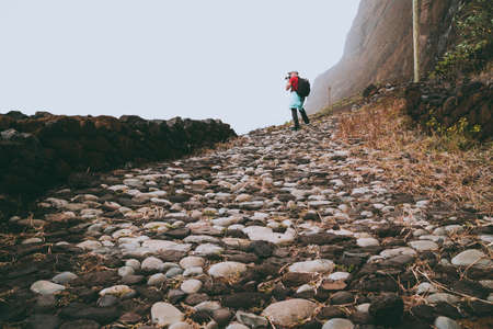Men hiker with backpack on the scenic coastal road. The route leads along huge volcanic rock cliffs above roaring ocean and joins the towns of Cruzinha and Ponta do Sol. Santo Antao. Cape Verdeの写真素材