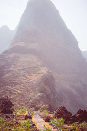 Ruin stone houses in arid landscape of amazing Aranhas valley. Hiking route to Ponta do Sol. Huge mountains of coastline and old local stone house in the background. Santo Antao Island, Cape Verdeの写真素材