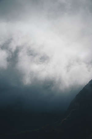 Moody scenery with mist flowing over huge mountain slope and spilling into the green valley. Santo...