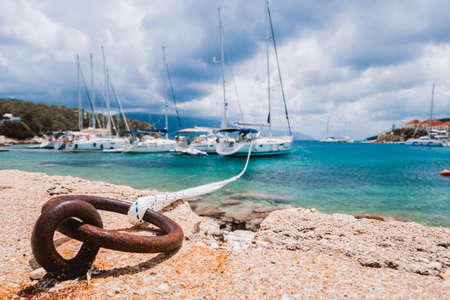 Mooring rope tied to rusty ring for rigging yachts in background. Wonderful view of port Fiskardo. Picturesque seascape of Ionian Sea. Outdoor scene of Kefalonia island, Greece, Europeの写真素材