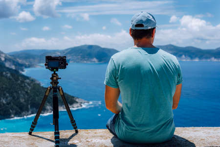 Travel Europe summer holiday in Greece. Happy man photographer enjoying cloudscape, coastline and Mediterranean sea visiting Kefalonia Island on cruise vacation. Camera on tripod capture timelapseの写真素材