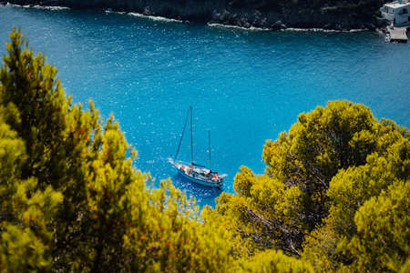 White yacht take a shelter in beautiful blue lagoon of Assos village Kefalonia. Frame between top of the green pine trees. Greeceの写真素材