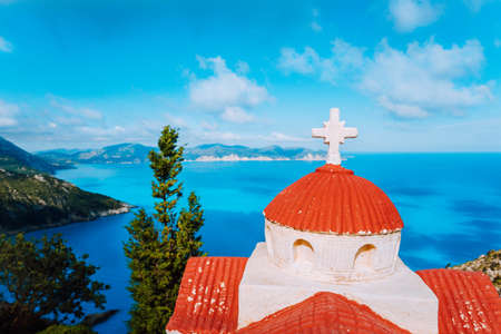 Orange colored Hellenic shrine Proskinitari on the cliff edge with defocused sea and cloudscape view in the backgroundの写真素材