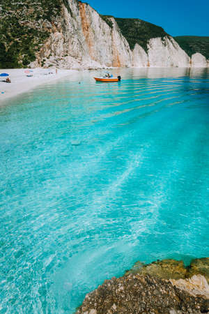 Tourist pleasure boat land to beautiful remote white pebble beach with rippled transparent clear blue sea water. Scenic landscape of rocky coastline in backgroundの写真素材