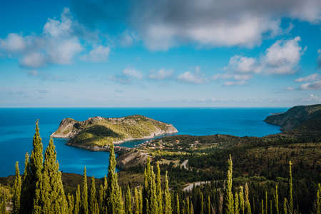 View to Assos village in sun light and beautiful blue sea. Green cypress trees in foreground. Kefalonia island, Greeceの写真素材