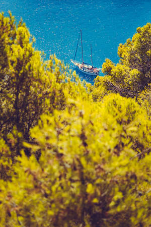White yacht take a shelter in beautiful blue lagoon of Assos village Kefalonia. Frame between top of the green pine trees. Greeceの写真素材